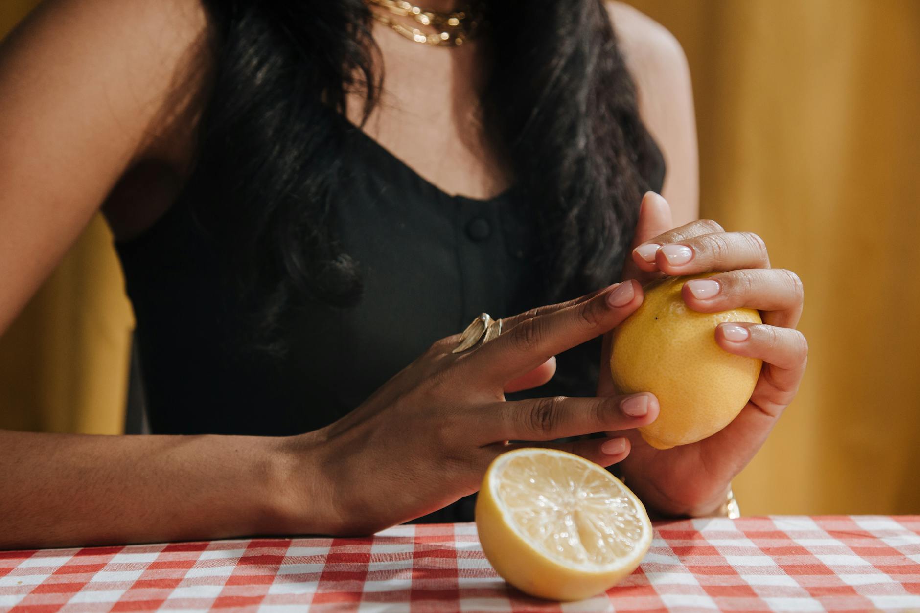 Woman holding a fresh lemon at a dining table, symbolizing natural, unhurried pleasure