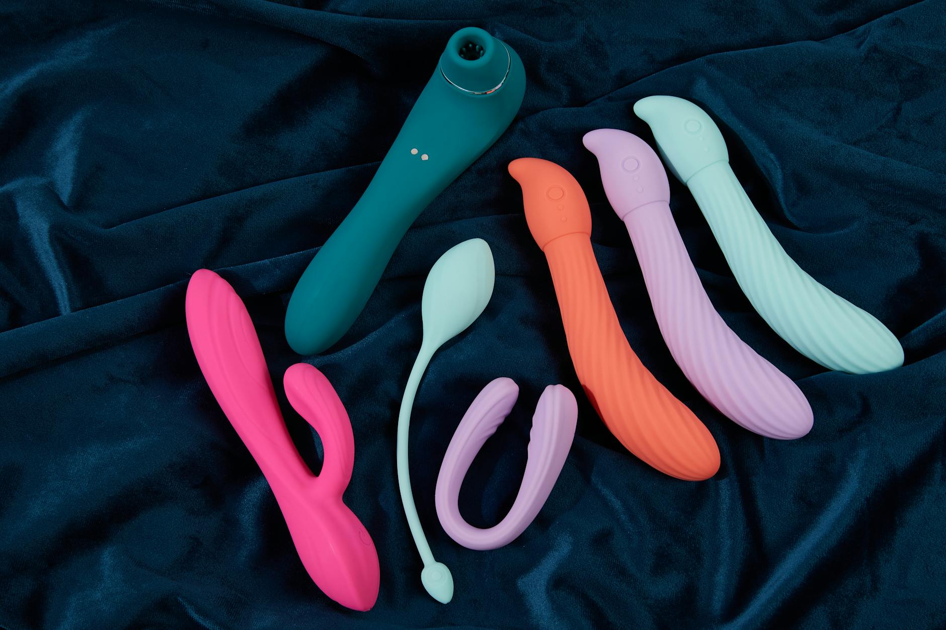 Collection of colorful silicone clitoral vibrators on dark fabric, including lemon-shaped designs