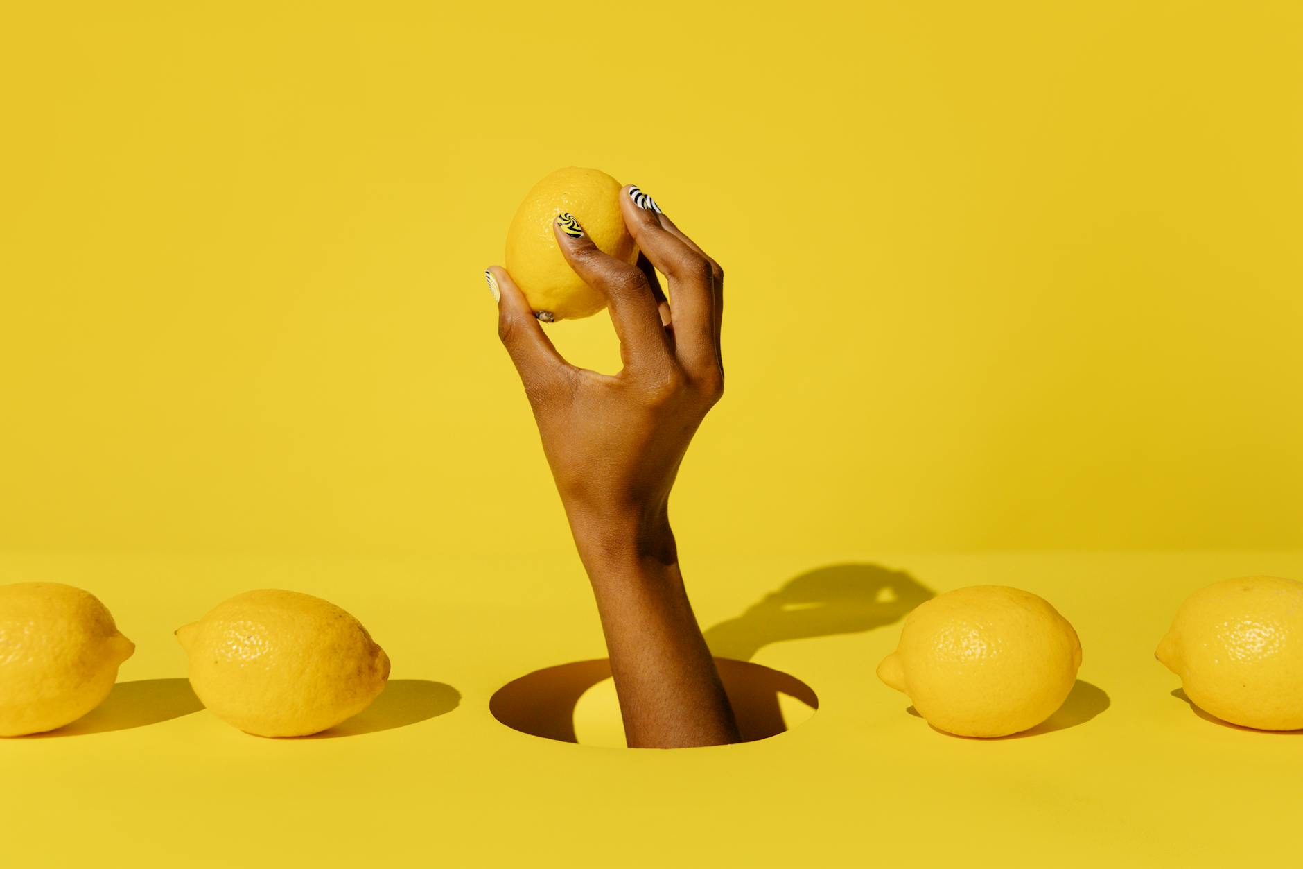 A hand holding a fresh lemon against a vibrant yellow background, symbolizing renewed vitality and sensation