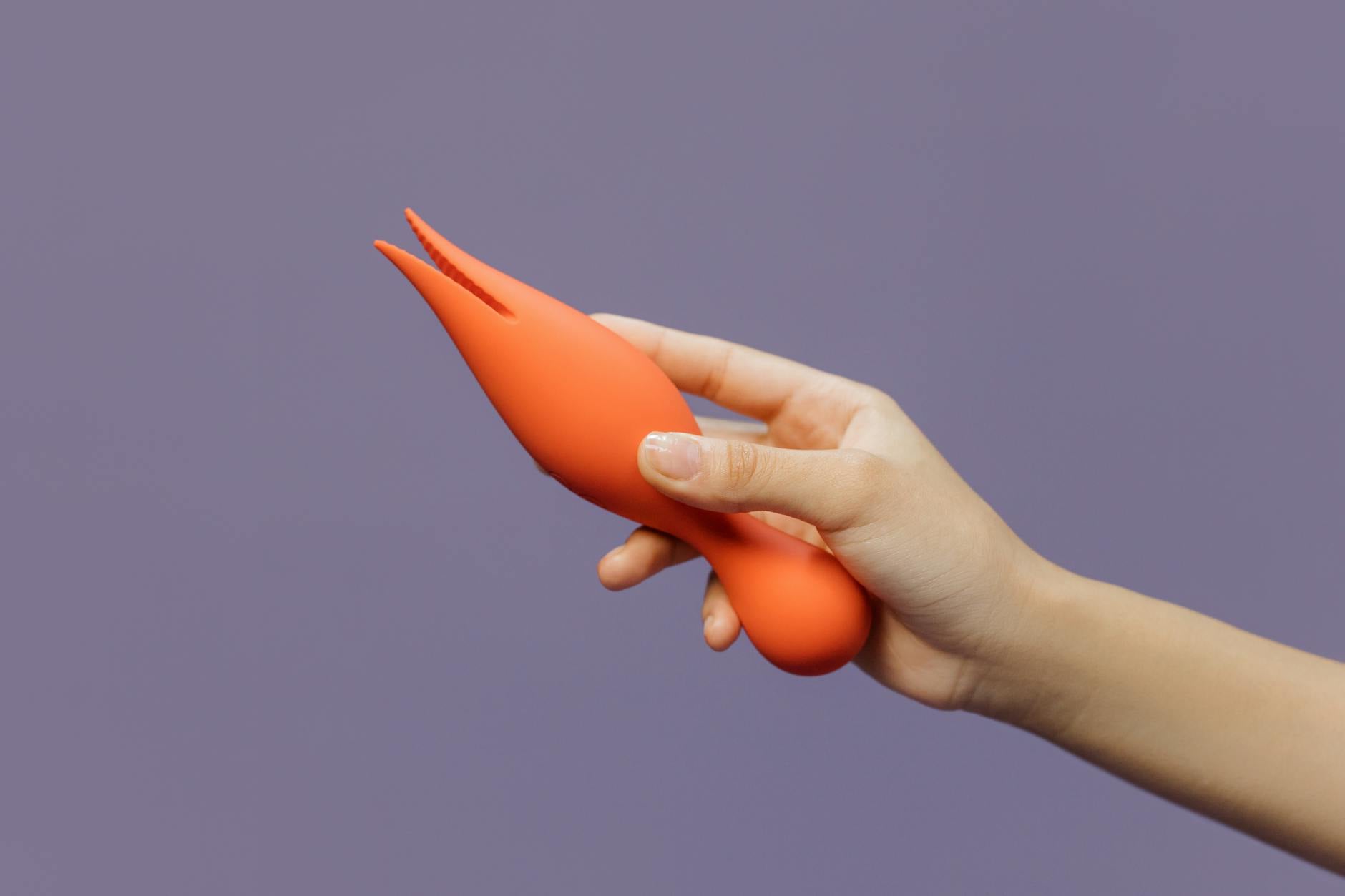 Close-up of a hand holding an orange lemon vibrator against a purple backdrop