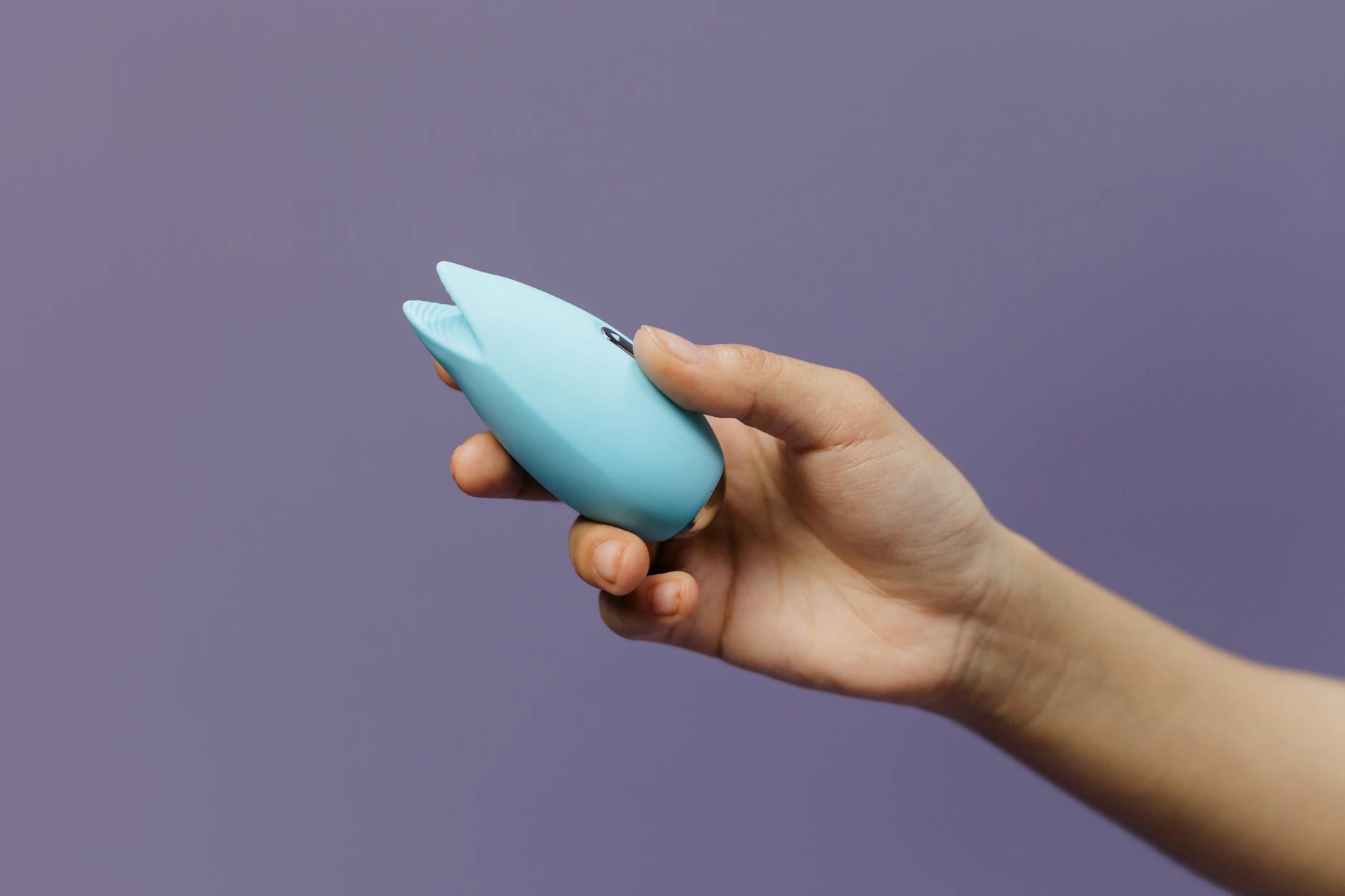 A blue silicone vibrator held in hand against a solid purple background, symbolizing self-love and reconnection with pleasure.
