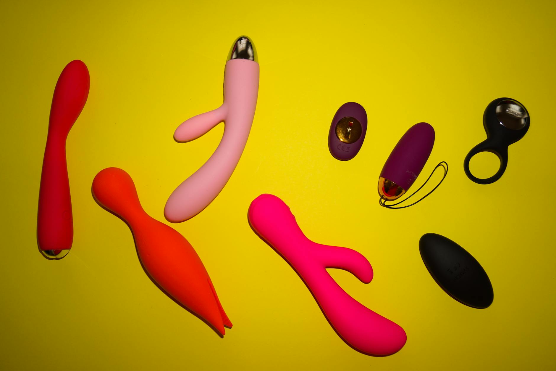Vibrant arrangement of various clitoral vibrators on a bright yellow surface, showcasing design and color diversity