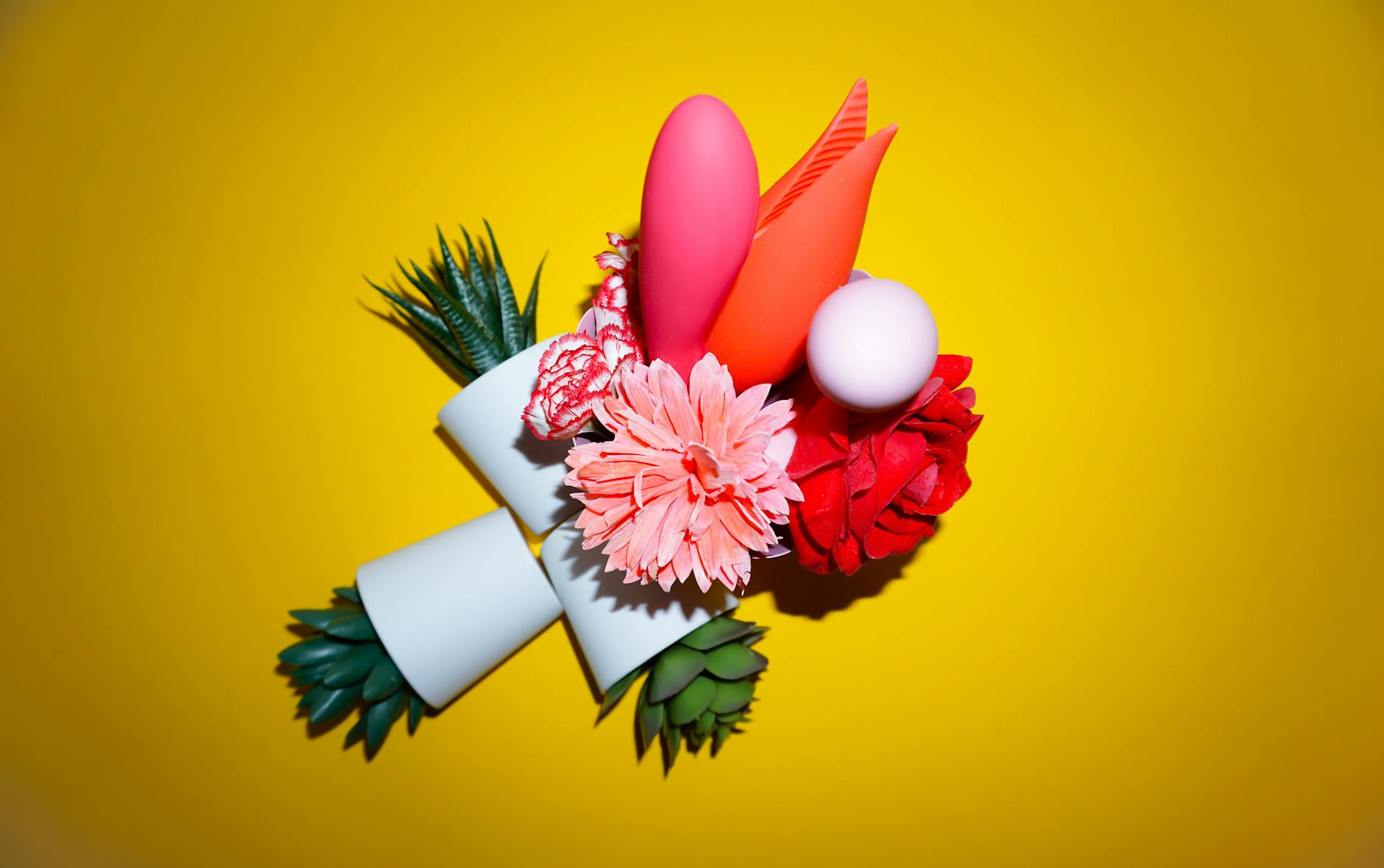 Two hands holding pink and blue silicone vibrators together on a pastel background, symbolizing shared pleasure and emotional connection.