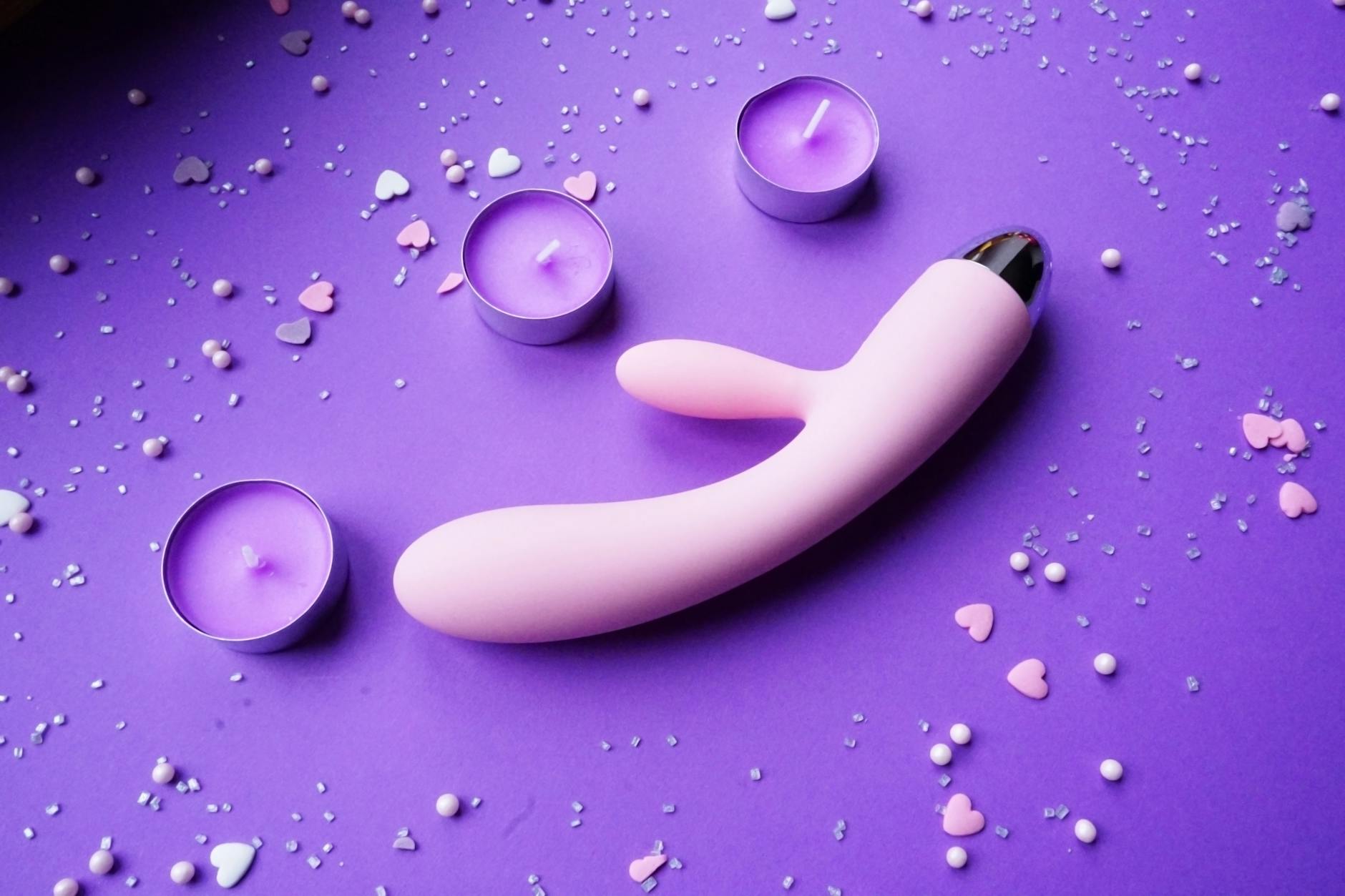 Vibrador de silicone colorido segurado na mão contra fundo roxo claro, representando intimidade moderna e exploração sexual